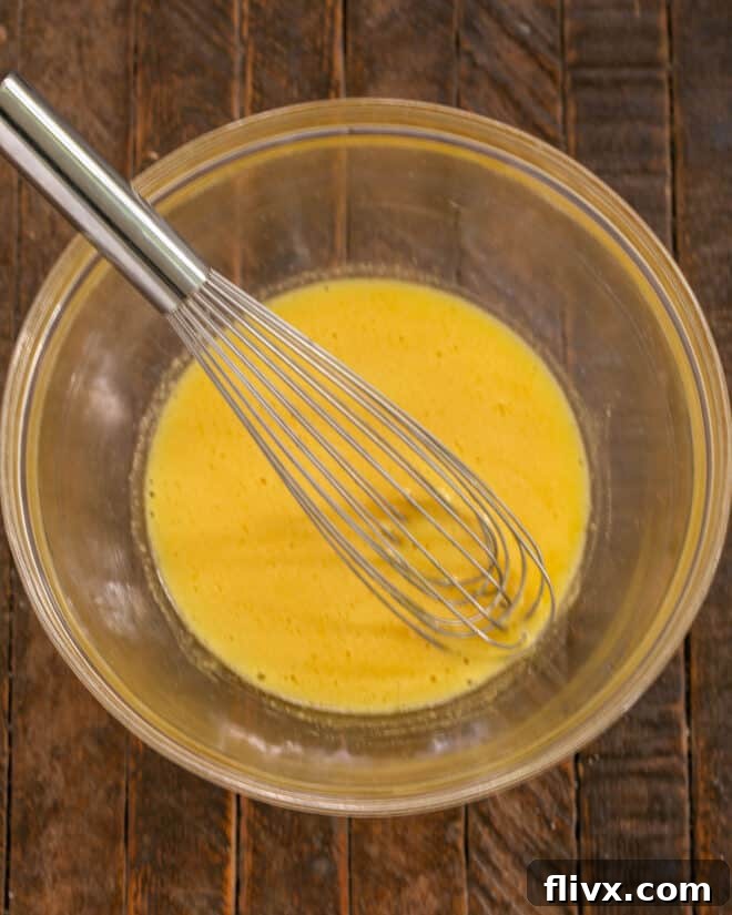 A bowl of egg yolks and granulated sugar being vigorously whisked together, creating a pale and creamy mixture.