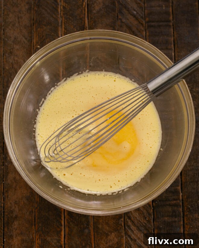 A chef actively tempering egg yolks by slowly whisking in hot cream, then cooking the mixture in a saucepan to thicken into a custard.