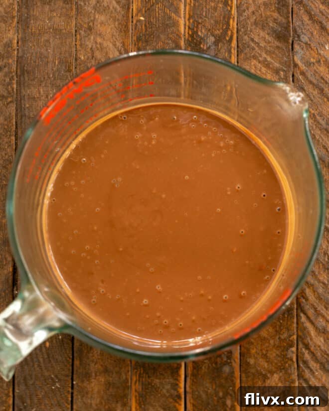 Warm custard being poured over chopped chocolate in a bowl, followed by whisking until the mixture is smooth and glossy.