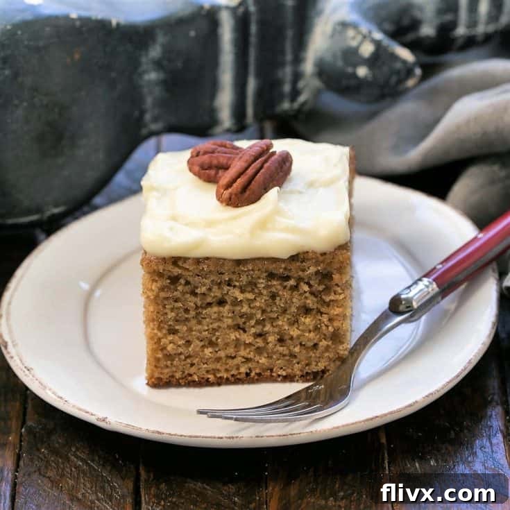 A slice of applesauce spice cake topped with 2 pecan on a round white plate with a red handled fork