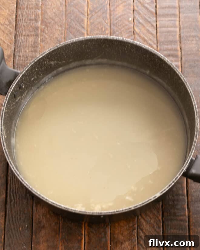 A rich, creamy white sauce simmering gently in a skillet, made from butter, flour, and chicken broth, forming the base of the Tetrazzini.