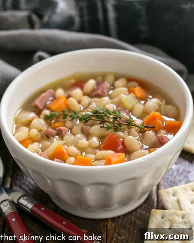 Navy bean soup in a white soup bowl with crackers and red handled spoons