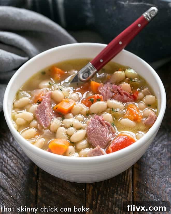 Old fashioned Navy Bean Soup in a white bowl with a red handled spoon