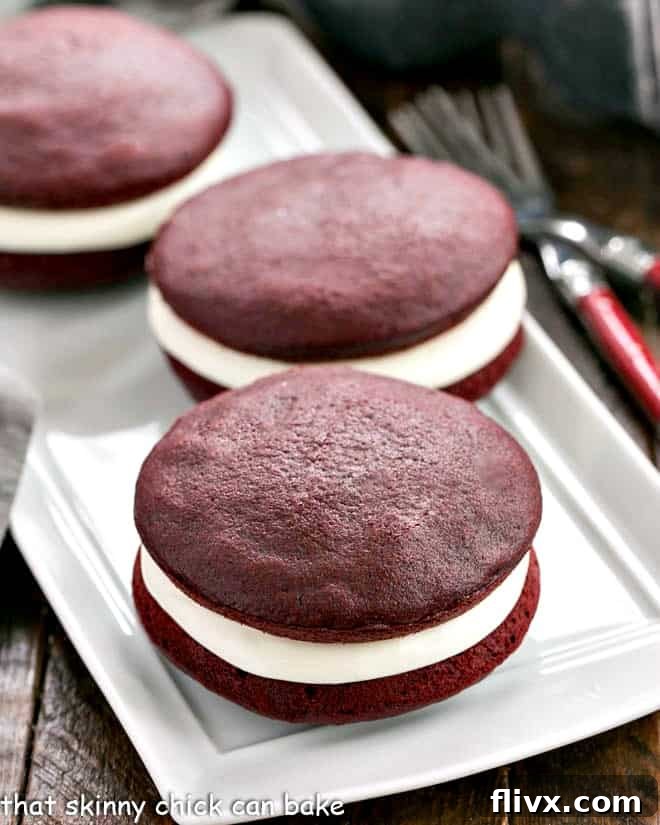 A selection of vibrant red velvet whoopie pies arranged neatly on a pristine white serving tray, showcasing their perfect dome shape and creamy filling peeking out.