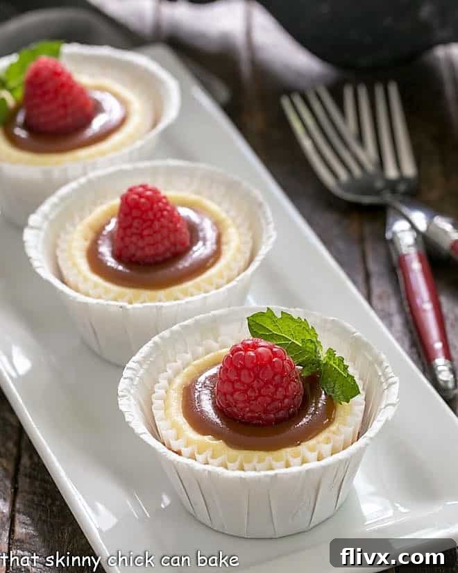 Caramel Topped Mini Cheesecakes on a white rectangular tray garnished with raspberries. The perfect individual dessert for any occasion.