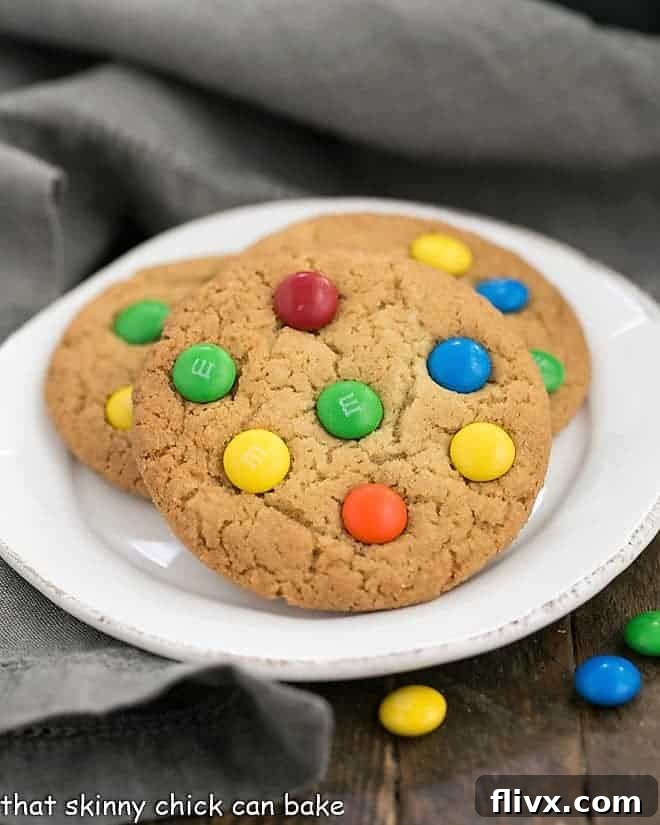 A stack of golden brown, chewy Classic M&M Cookies dotted with colorful candies, arranged on a round white plate.