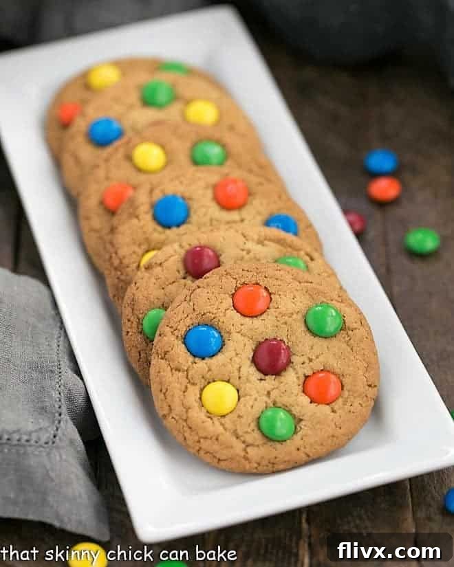 A perfect line of Classic M&M Cookies arranged neatly on a sleek white rectangular tray, showcasing their vibrant colors and appealing texture.