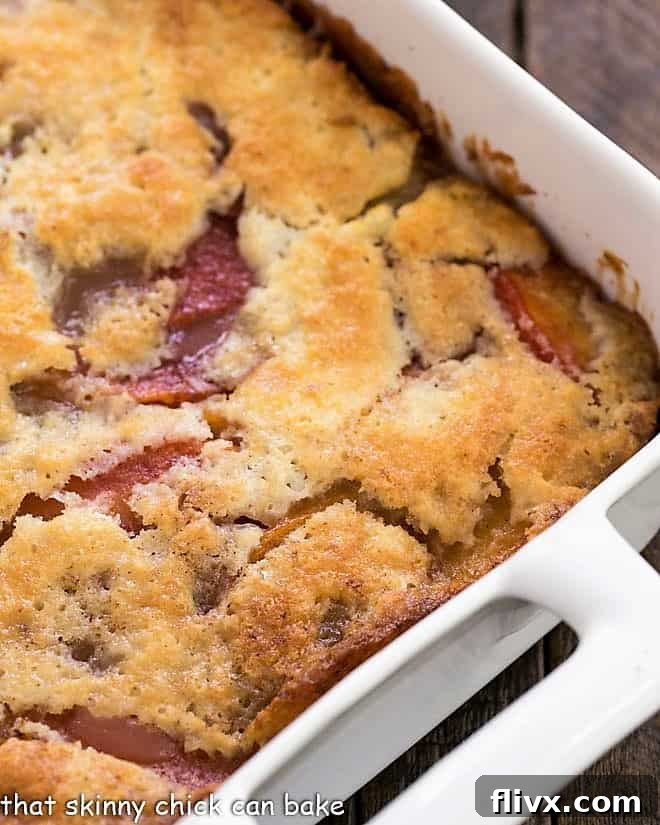 A close-up view of a freshly baked easy peach cobbler cooling in a white ceramic baking dish, showing its bubbly, golden-brown crust and juicy peach filling.