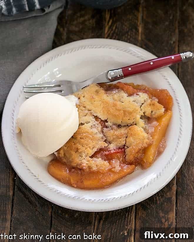 Overhead view of an easy peach cobbler topped with a scoop of vanilla ice cream with a red handled fork