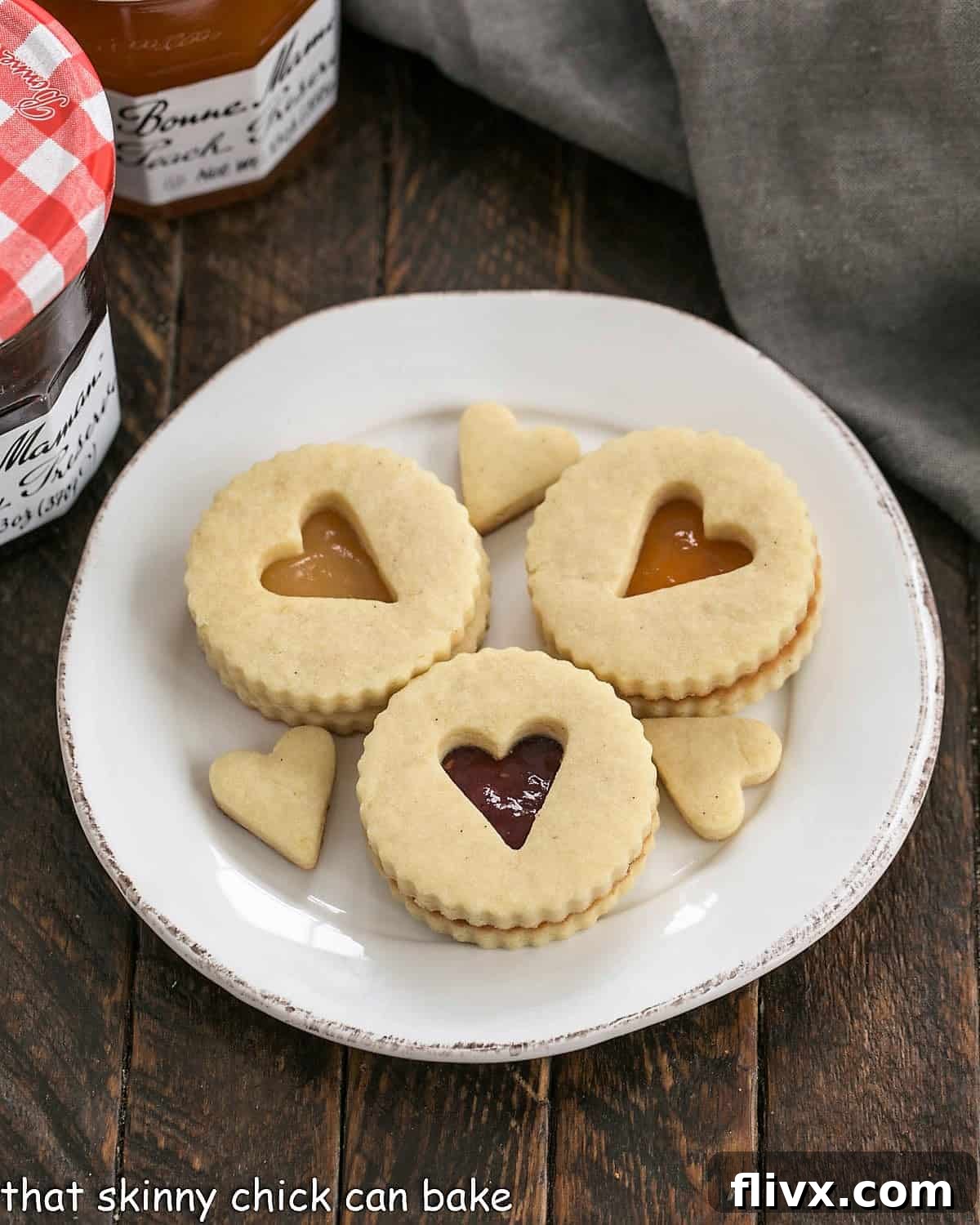 Overhead view of 3 linzer cookies and their small cutouts on a round white plate, emphasizing the intricate details.