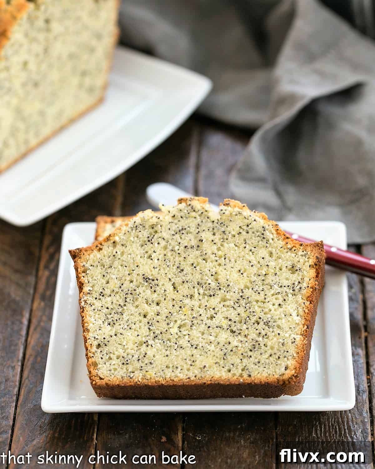 Sunshine Lemon Poppy Seed Loaf 3 Two perfectly cut slices of lemon poppy seed tea cake on a square white plate with a red handled knife resting in front of the remaining loaf on a ceramic tray.
